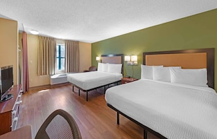 Habitación de hotel con dos camas, un escritorio con televisor y una ventana con cortinas.