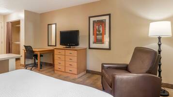 A hotel room with a bed, a desk with a television, a chair, a dresser, and a lamp.
