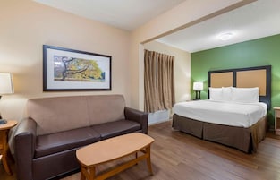 Habitación de hotel con cama, sofá, una mesita, un cuadro en la pared y una ventana con cortinas.