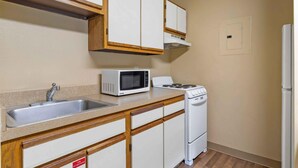 Een kitchenette met een magnetron, fornuis, spoelbak en houten kastjes.