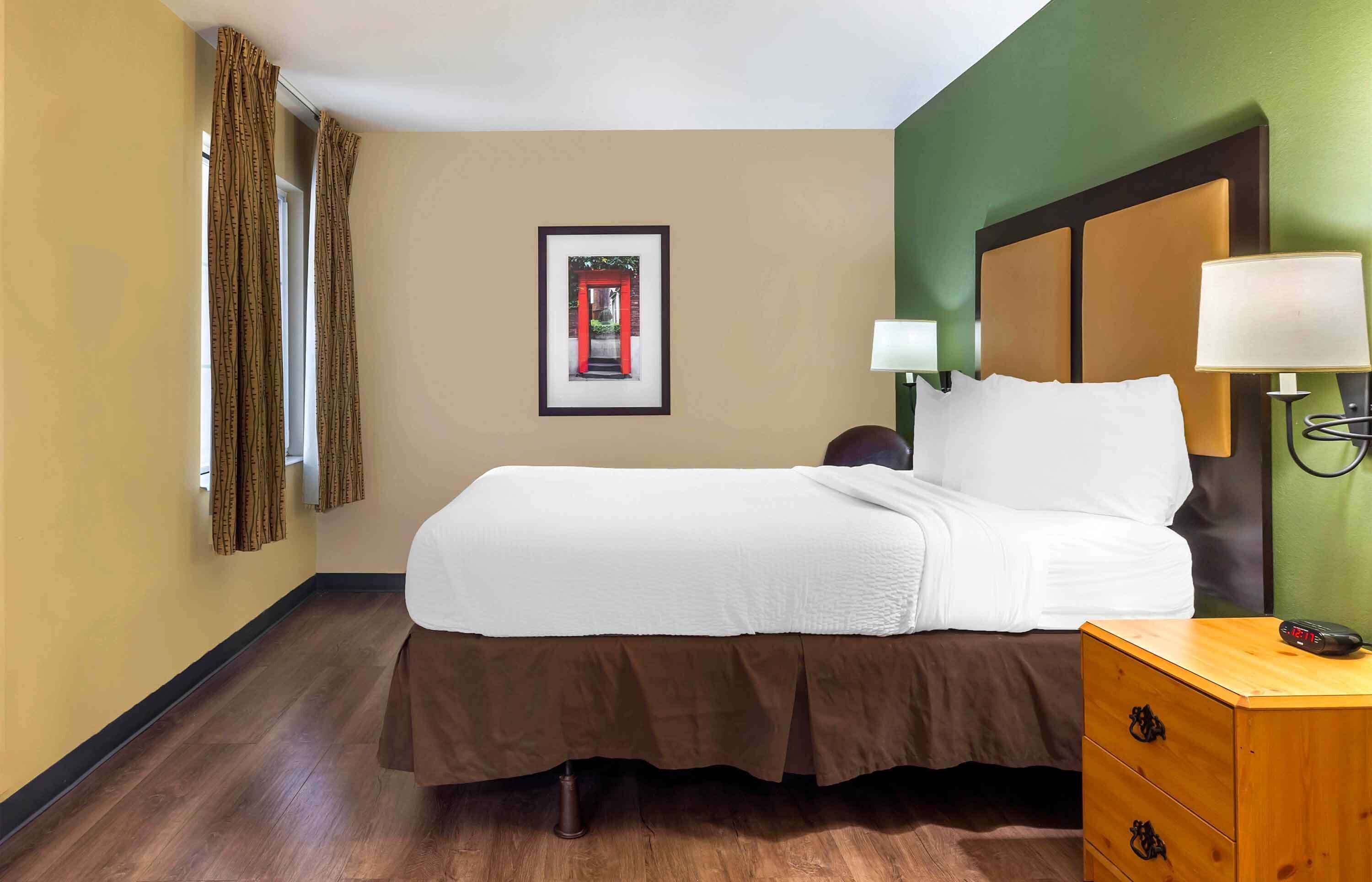 Una habitación de hotel con una cama, una mesita de noche, una lámpara y un cuadro en la pared.