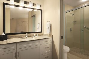 A bathroom with a large mirror, a sink, a toilet, and a glass-enclosed shower.
