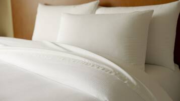 A neatly made bed with white linens and pillows, a wooden headboard, and a textured blanket.