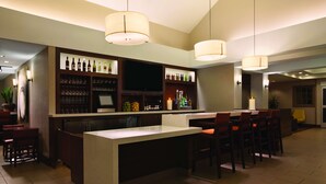 A bar area with a counter, bar stools, and shelves stocked with bottles and glasses. - HYATT house Pleasanton (Pleasanton)