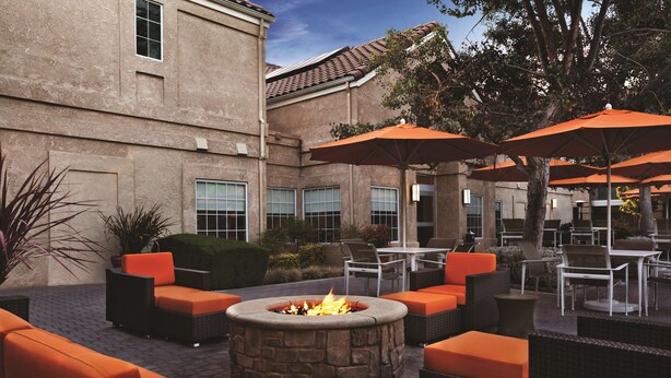 An outdoor patio area with stone fire pit, orange seating, and umbrellas. - HYATT house Pleasanton (Pleasanton)