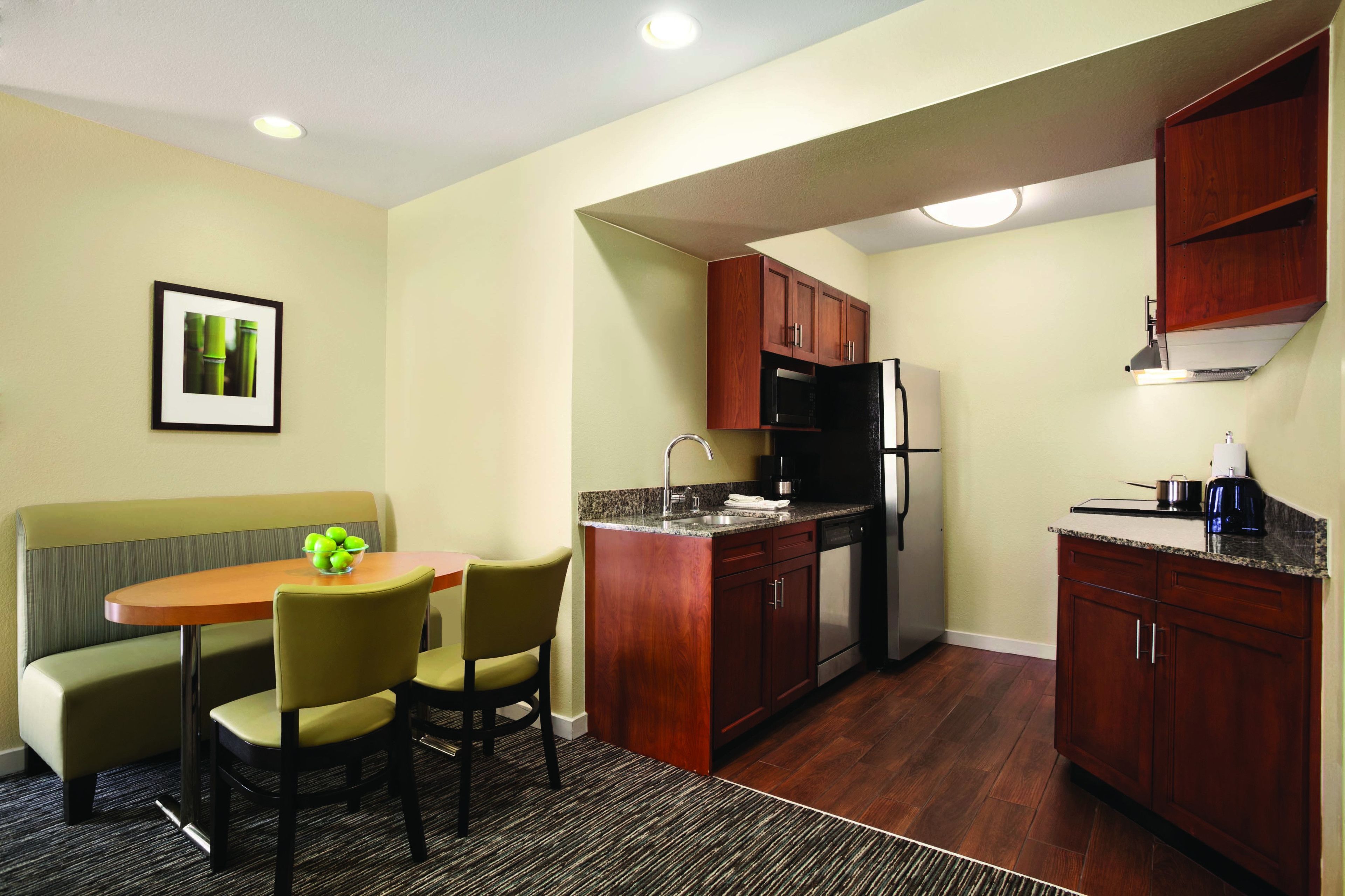 A compact kitchen with wooden cabinets, a built-in microwave, and a refrigerator. There is a dining area with a small table and chairs.