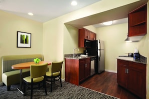 A compact kitchen with wooden cabinets, a built-in microwave, and a refrigerator. There is a dining area with a small table and chairs.