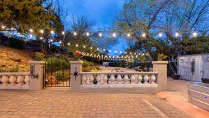 A paved entrance with a gate, string lights, and a sign indicating a garden area. - Cedars Resort (Sedona)
