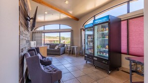 A modern lounge area with a sofa, chairs, a small table, a refrigerator, and large windows offering a view. - Cedars Resort (Sedona)