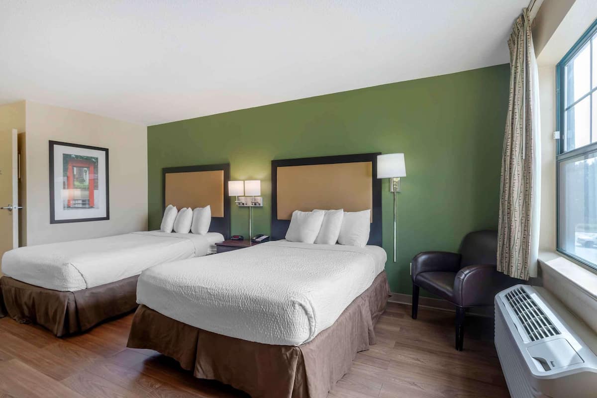 Ein Hotelzimmer mit zwei Betten, einem Schreibtisch, einem Stuhl, einem Fenster mit Vorhängen und einem Wandheizkörper.