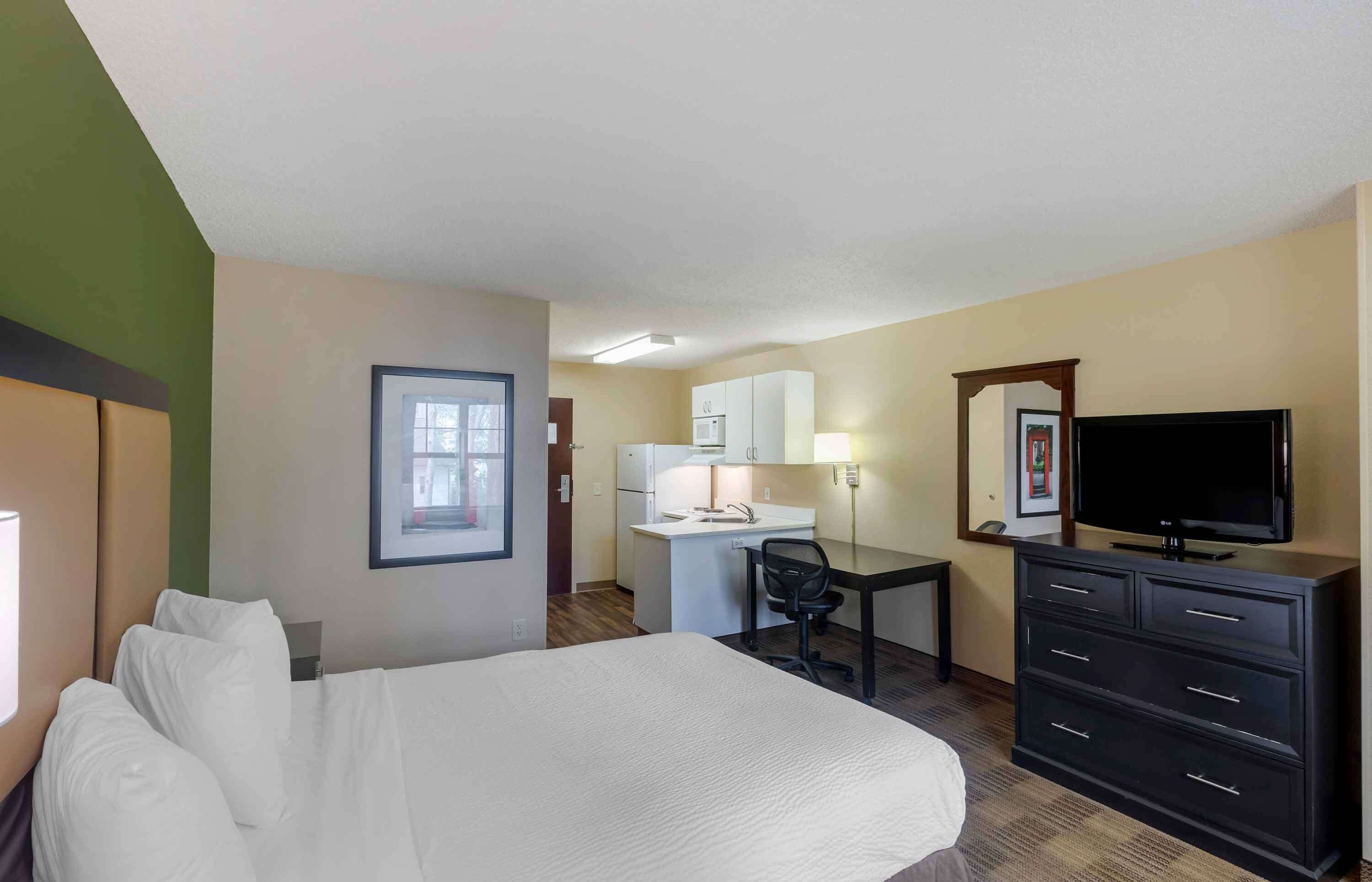 Habitación de hotel con cama, escritorio con silla, televisor y cómoda.
