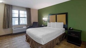 Habitación de hotel con una cama grande, una silla, una mesita de noche, una lámpara y un ventanal con cortinas.