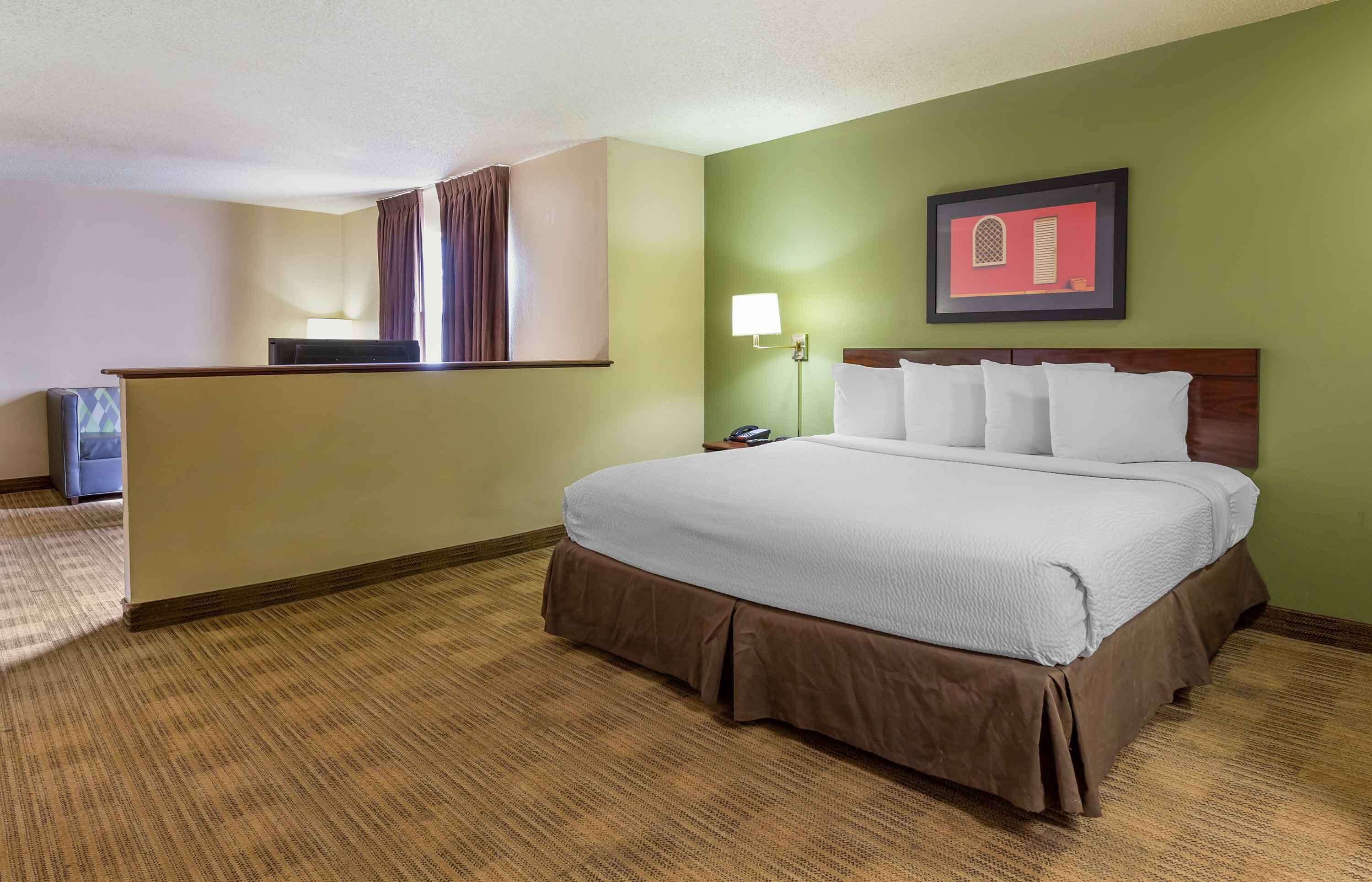 A hotel room with a large bed, a desk, a chair, and a nightstand.