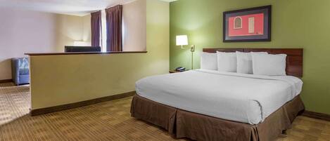 A hotel room with a large bed, a desk, a chair, and a nightstand.