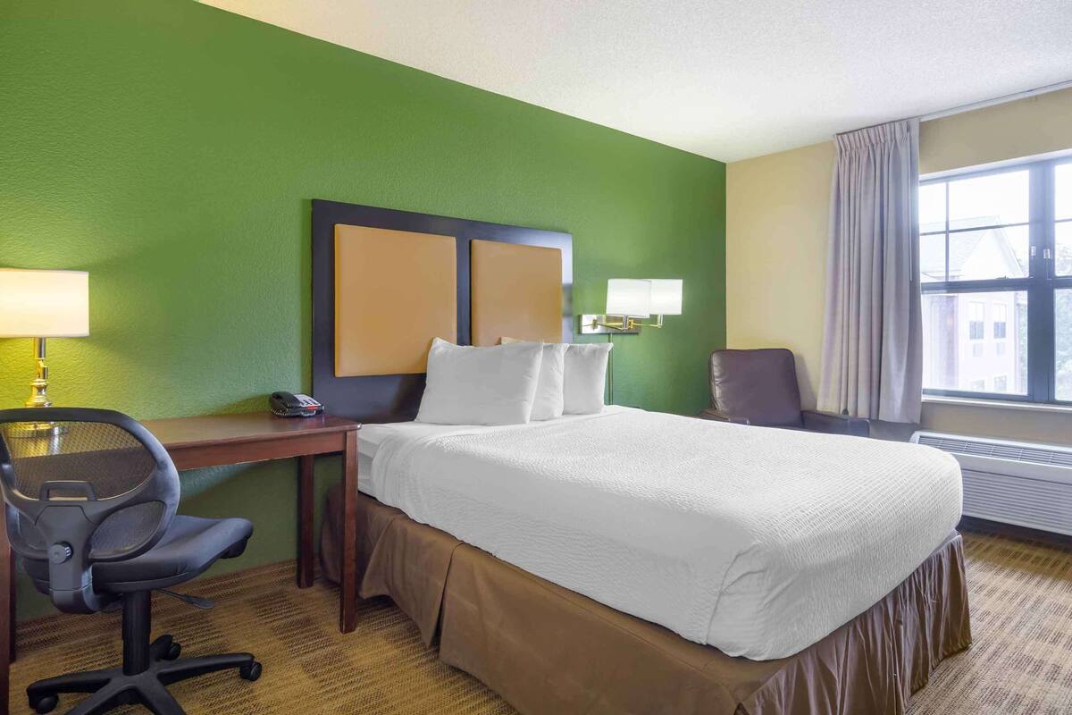 Habitación de hotel con una cama grande, un escritorio con silla, un teléfono y una lámpara.