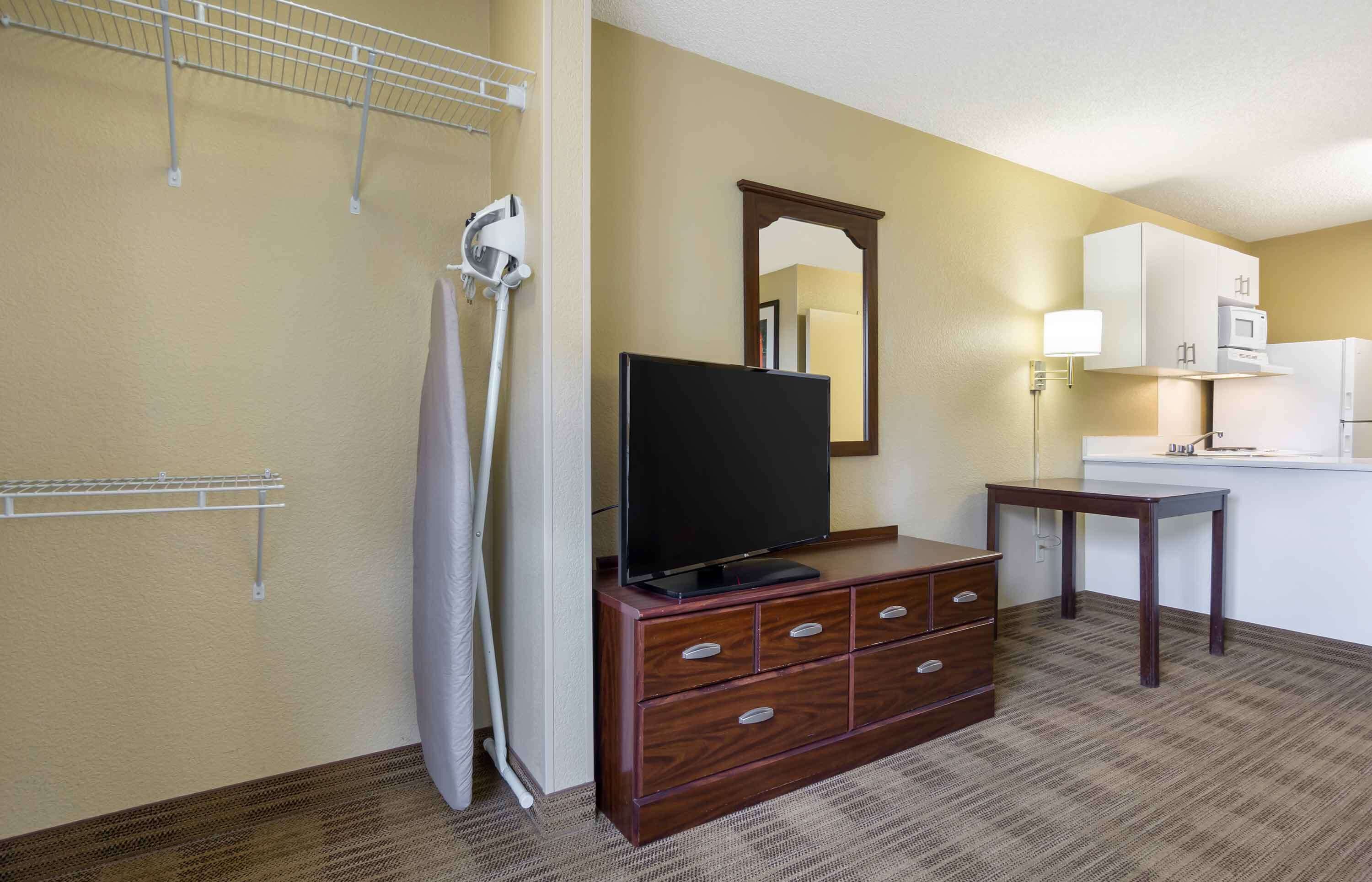 A hotel room with a wooden dresser, a flat-screen TV, a mirror, a small table, and a microwave.