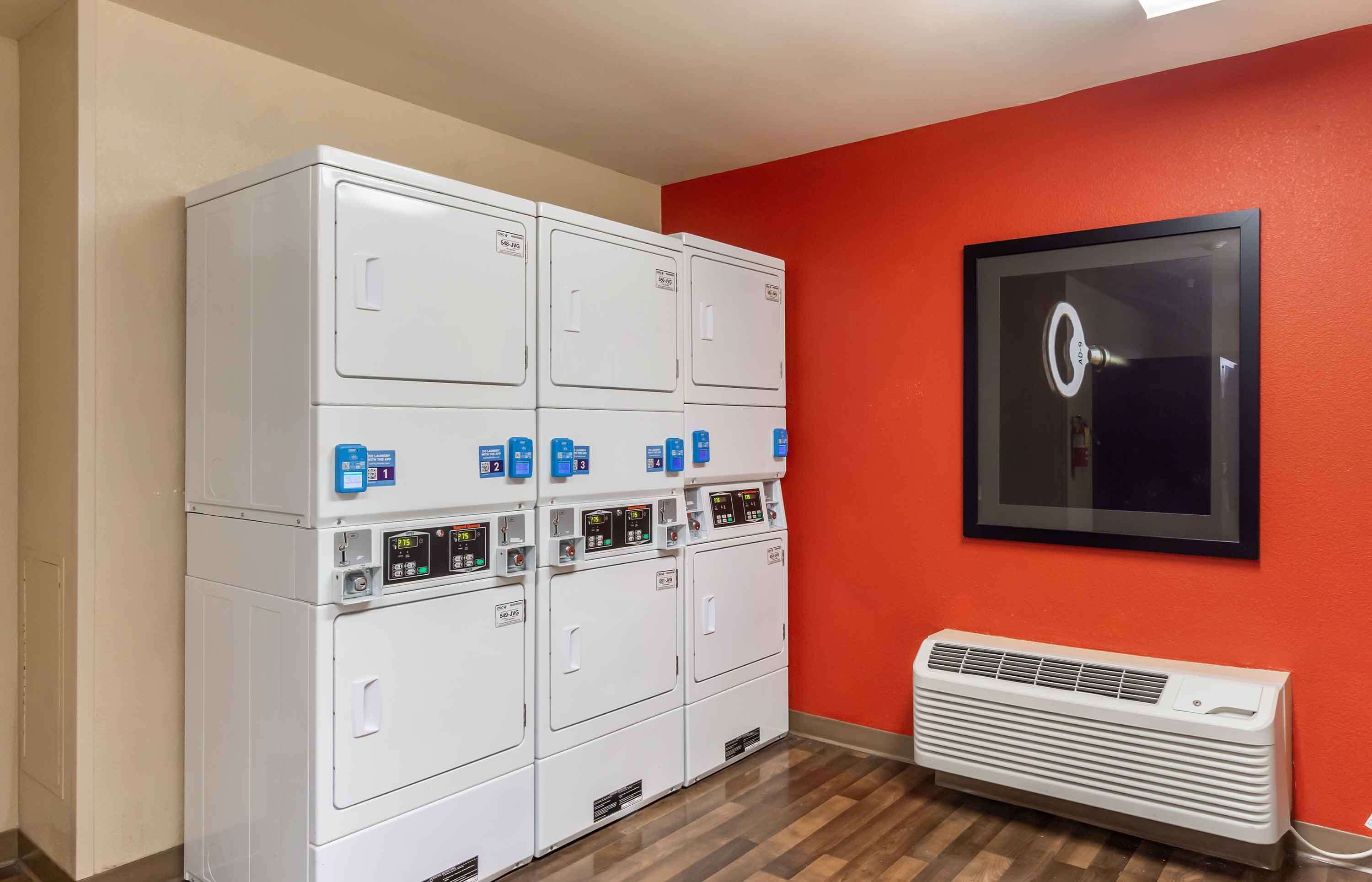 A laundry room with stacked dryers and a wall-mounted air conditioner.