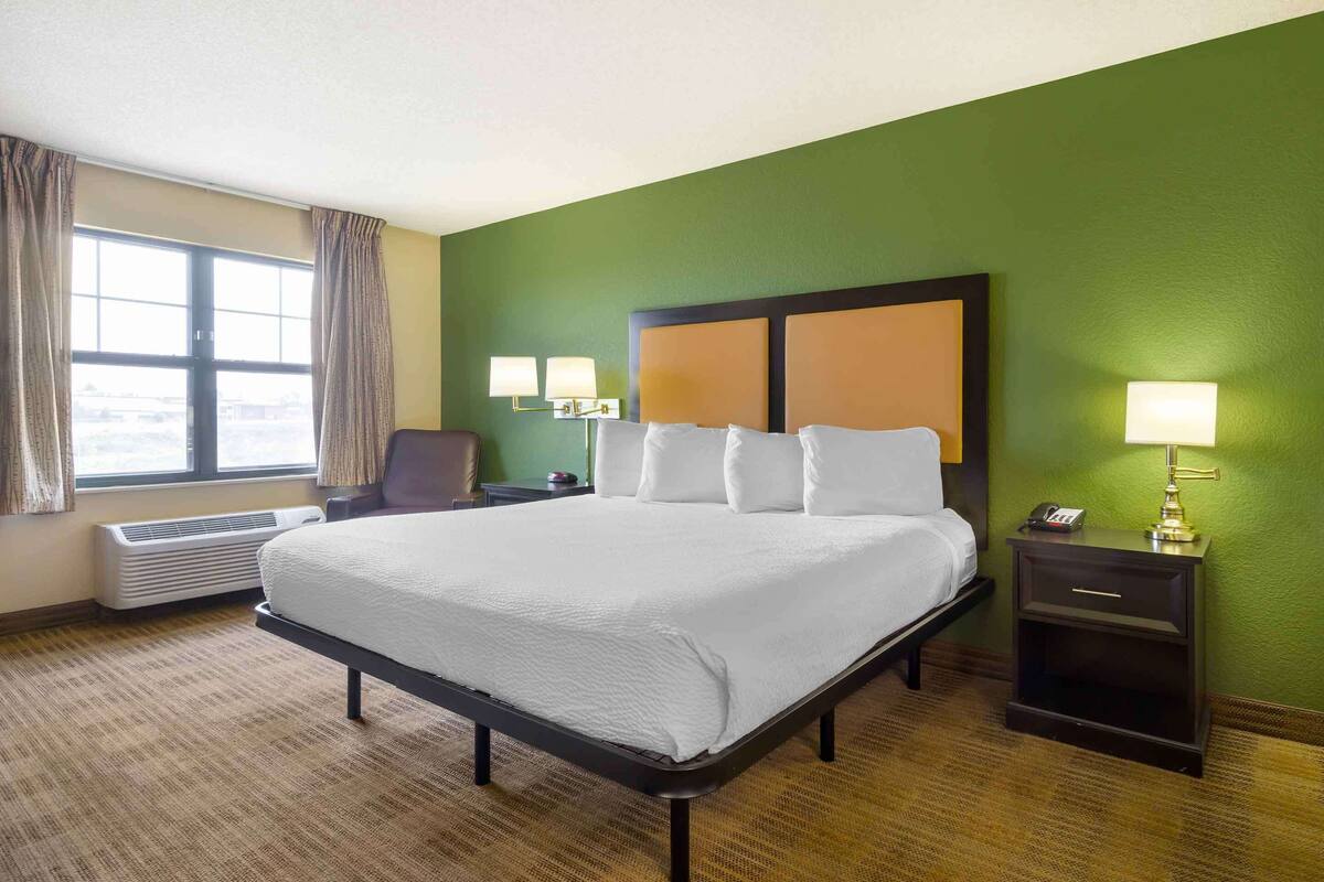 Habitación de hotel con una cama grande, dos lámparas de noche, una mesita de noche, una silla y un ventanal con cortinas.