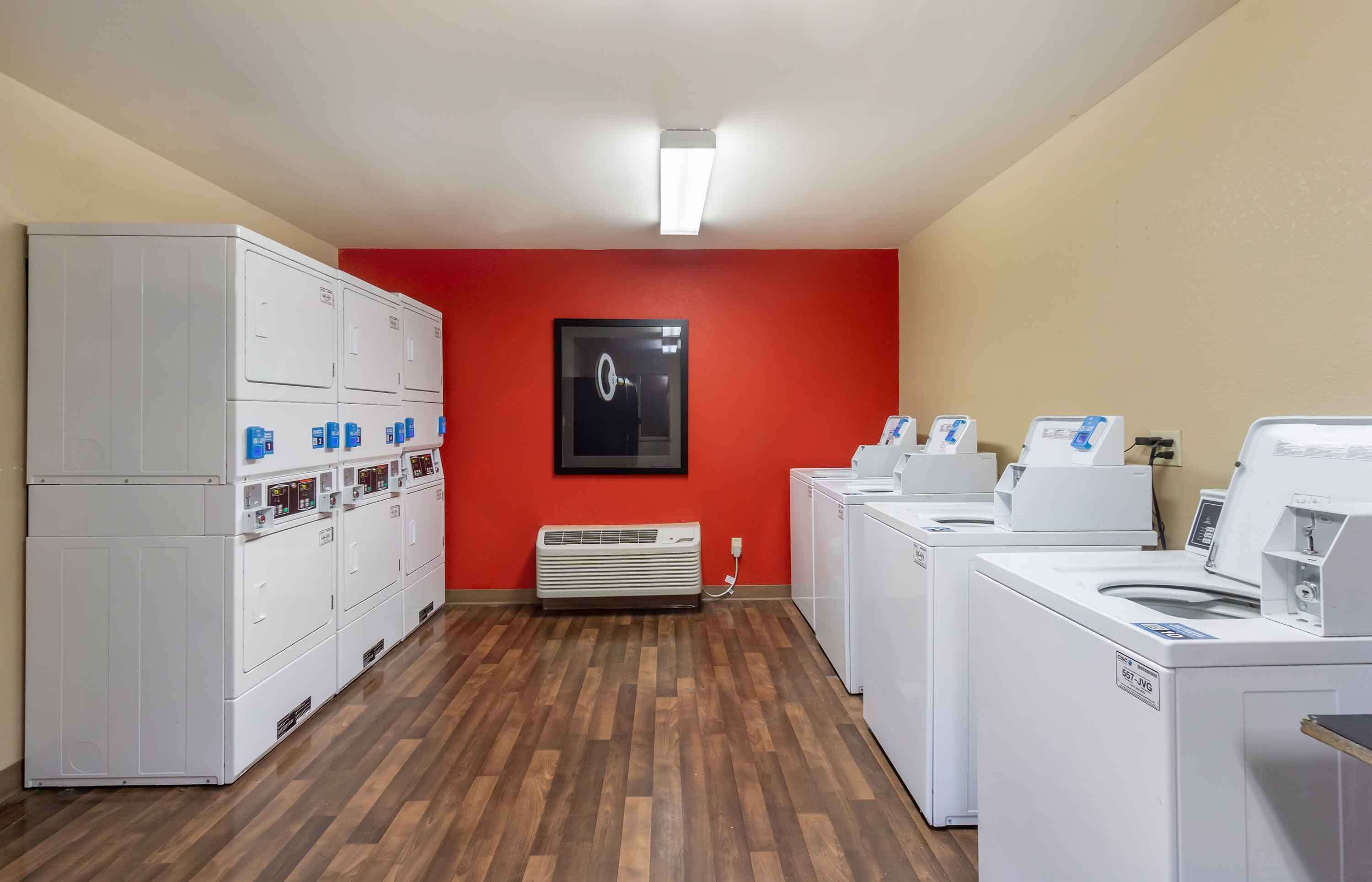 A laundry room with multiple washing machines and dryers, a red wall, and a ceiling light.