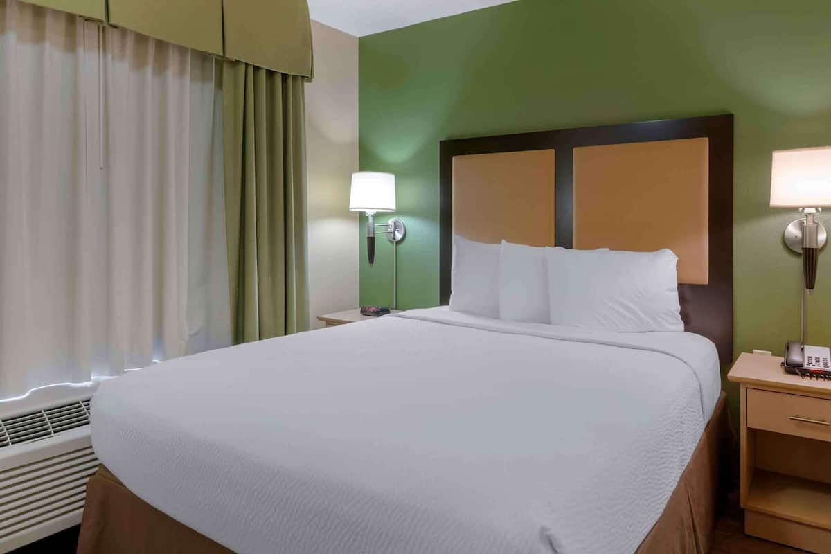 A hotel room with a large bed, two bedside tables with lamps, a heater, and a window with curtains.
