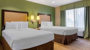 A hotel room with two beds, green walls, and a large window with curtains.