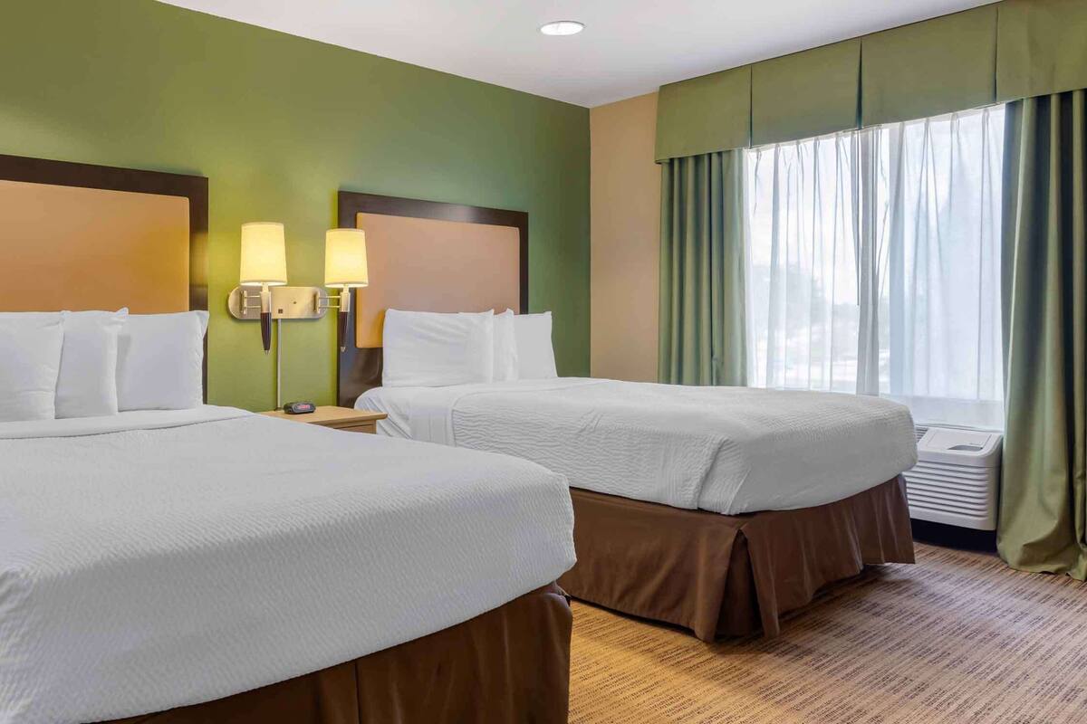A hotel room with two beds, green walls, and a large window with curtains.