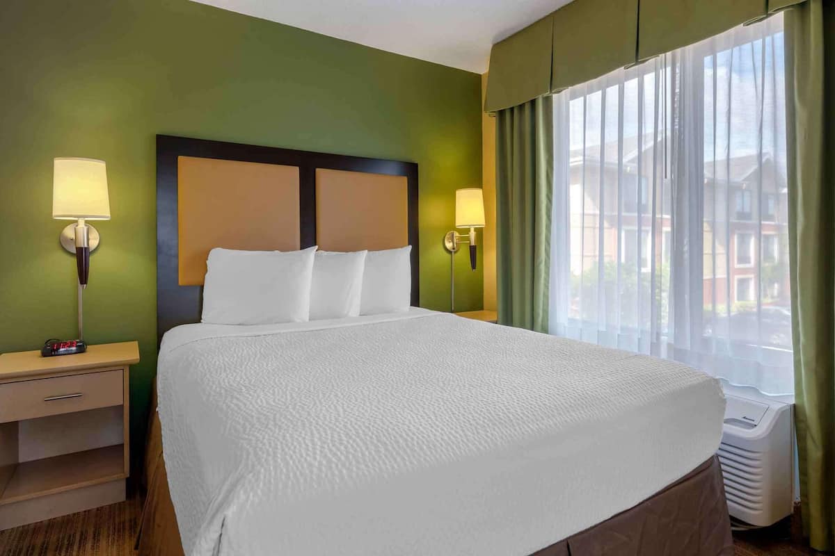 A hotel room with a bed, nightstands, lamps, and a window with curtains.