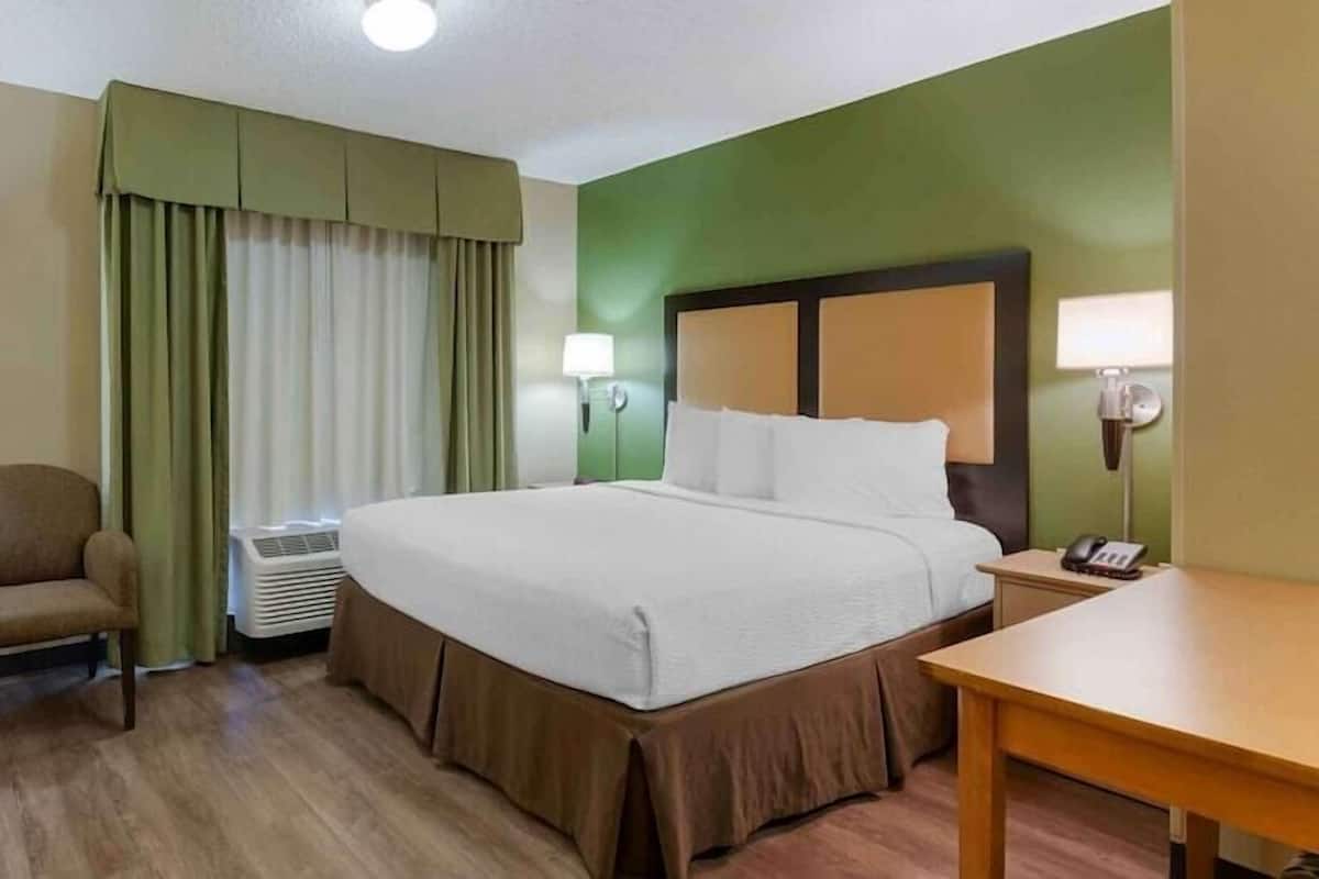 A hotel room with a bed, a chair, a desk, a television, and a telephone.