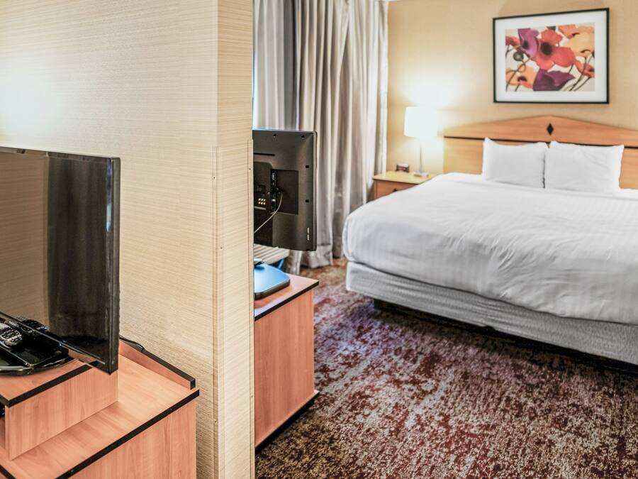 A hotel room with a bed, a desk with a flat-screen TV, a telephone, and a lamp.
