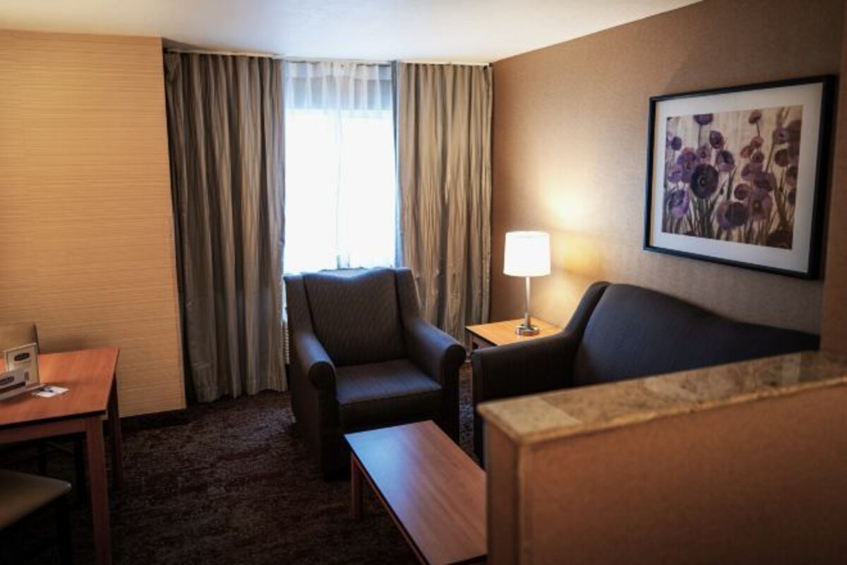 A hotel room with a sofa, armchair, table, lamp, and a framed picture on the wall.