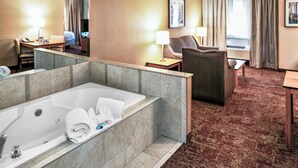 Habitación de hotel con una bañera grande, un escritorio con lámpara, una silla y una cama.