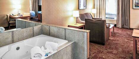 A hotel room with a large bathtub, a desk with a lamp, a chair, and a bed.