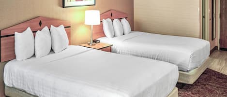 A hotel room with two beds, a nightstand, a lamp, a framed picture on the wall, and a door.