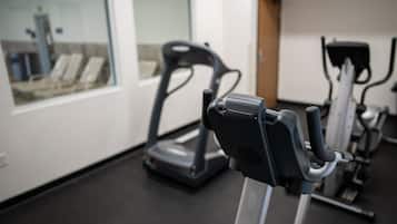 Un gimnasio con equipo de ejercicio, incluyendo cintas de correr y bicicletas estáticas, y un ventanal con vistas a un edificio.