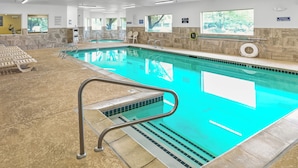 Una piscina interior con agua cristalina, una silla de socorrista y un flotador en la pared.