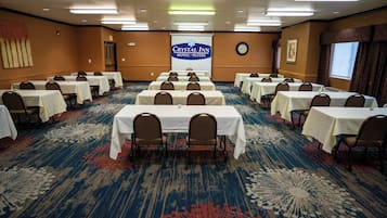 A conference room with multiple tables and chairs, a large banner with the hotel name, a clock, and a window with curtains.