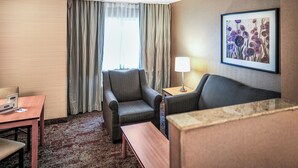 Una habitación de hotel con sofá, sillón, mesita y lámpara.
