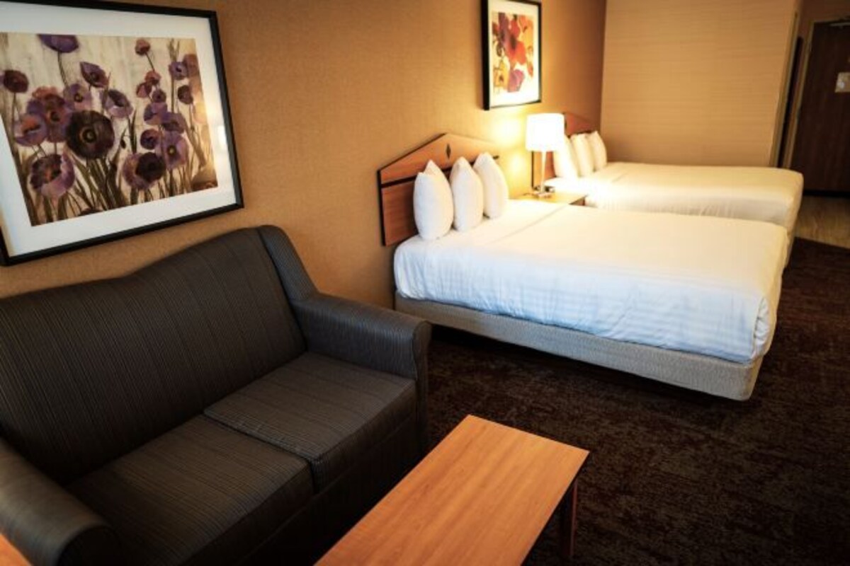 A hotel room with a sofa, two beds, a nightstand, and framed artwork on the wall.
