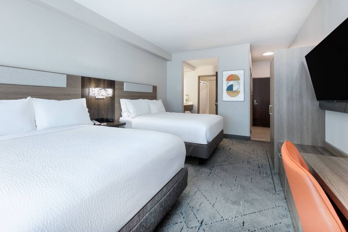 A hotel room with two beds, a TV, and a shower area.