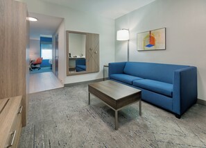 A modern room with a blue sofa, a wooden coffee table, a floor lamp, and a painting on the wall. - Holiday Inn Express & Suites Dallas Park Central Northeast by IHG (Dallas)