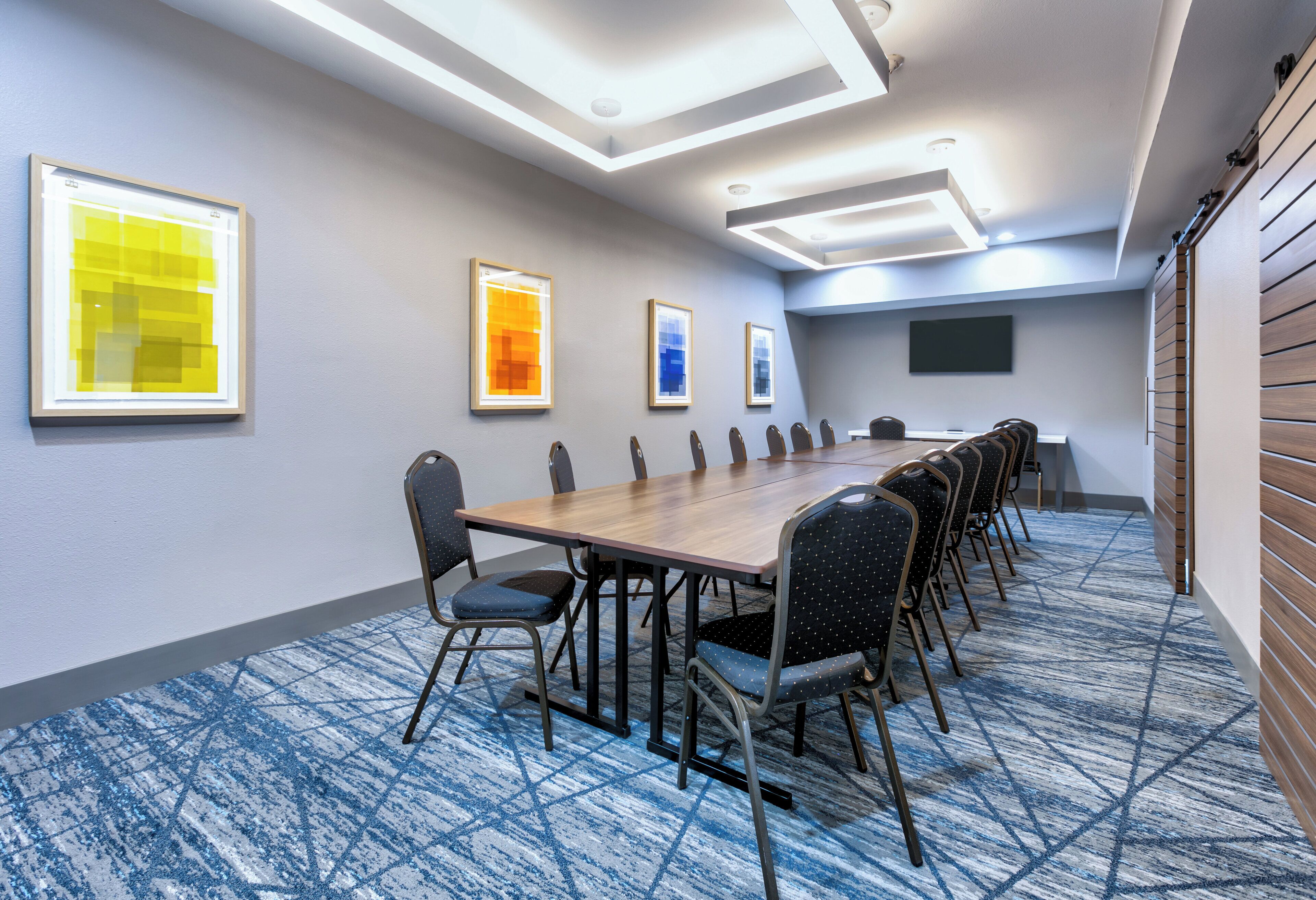 A conference room with a long table, chairs, framed artwork on the walls, and a carpeted floor.