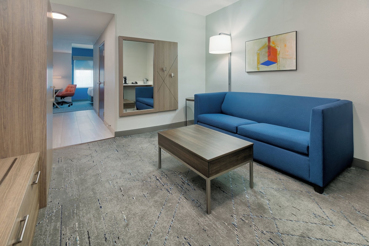 A modern room with a blue sofa, a wooden coffee table, a floor lamp, and a large mirror.