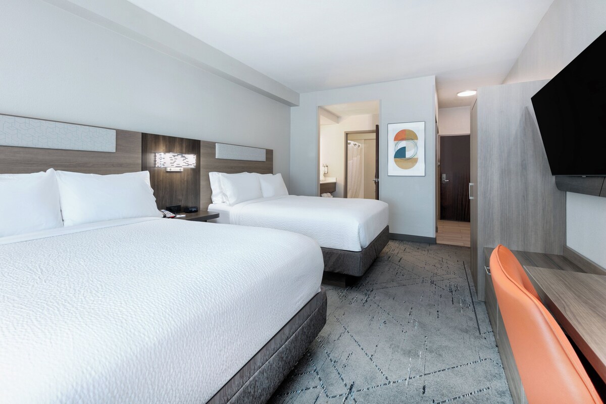A hotel room with two beds, a TV, and a shower area.