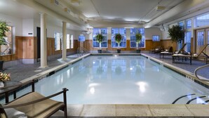 An indoor swimming pool with clear water, wooden paneling, and large windows. - Green Mountain Suites Hotel (South Burlington)