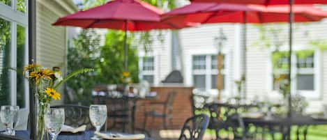 An outdoor patio with round tables, red umbrellas, and a vase with flowers.