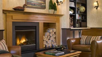 A cozy living room with a fireplace, leather sofas, a coffee table, and a bookshelf filled with books and decorative items.