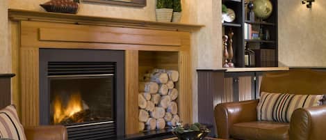 A cozy living room with a fireplace, leather sofas, a coffee table, and a bookshelf filled with books and decorative items.