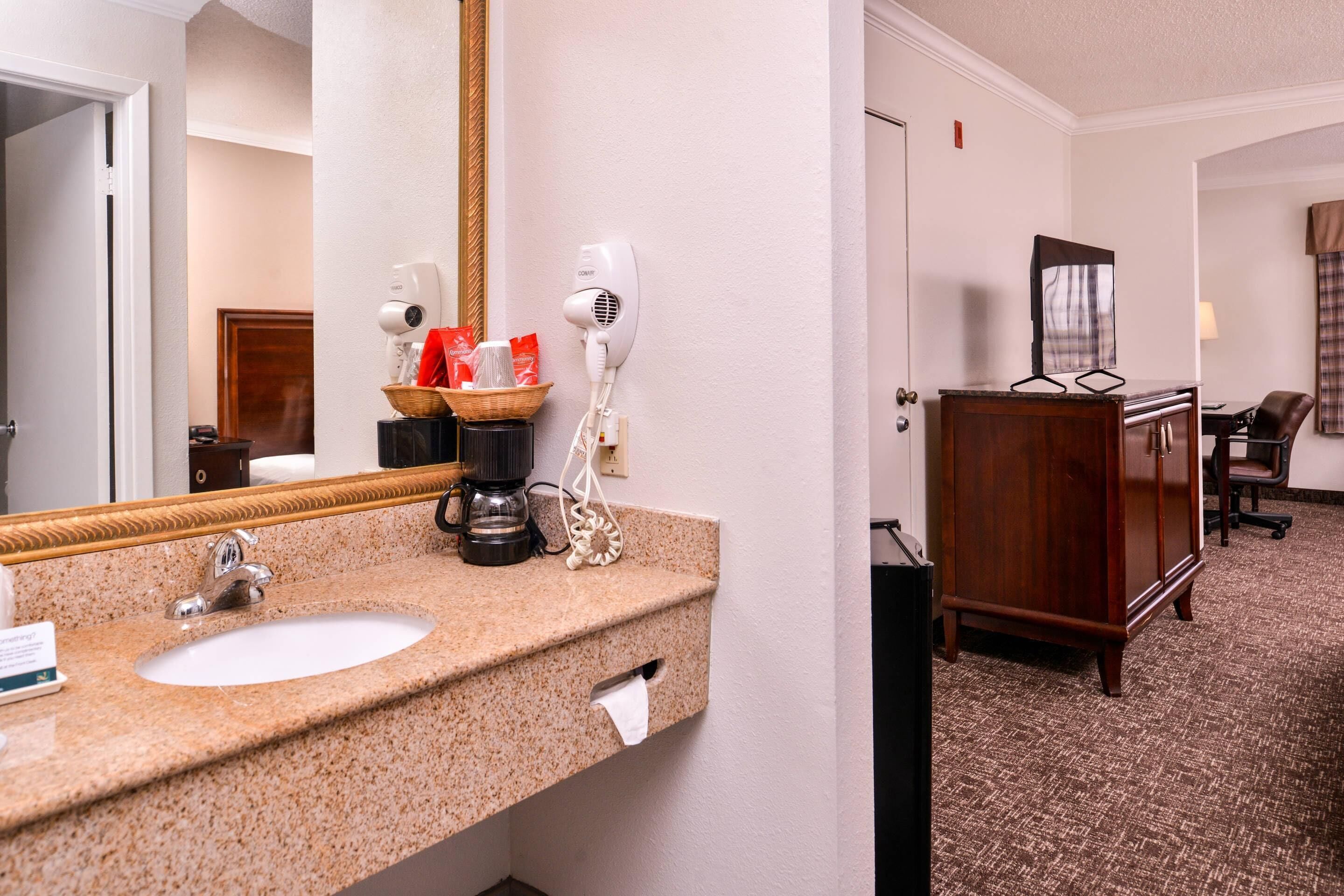 A hotel bathroom with a granite sink, two hair dryers, a coffee maker, and a mirror.