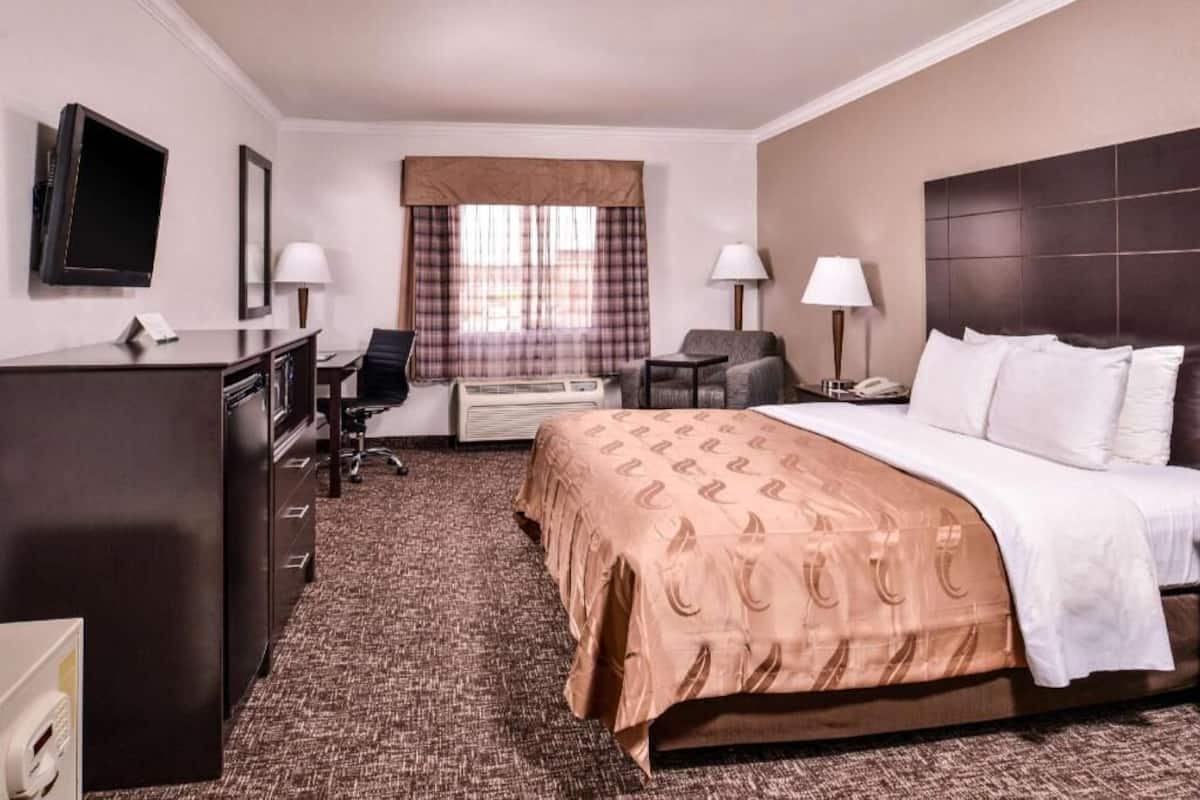 A hotel room with a bed, desk, chair, TV, and window with curtains.