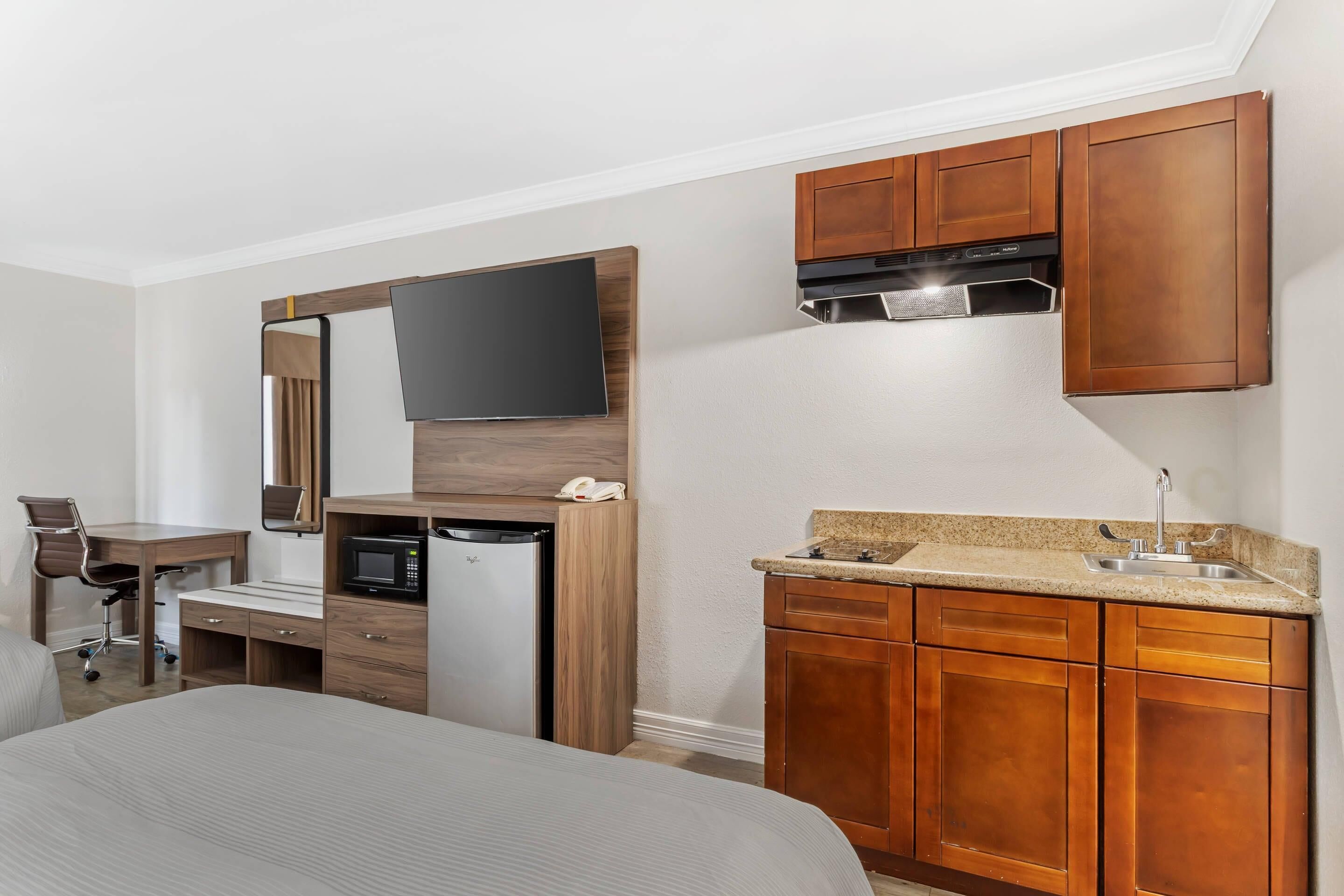 A compact hotel room with a kitchenette, a bed, a desk, and a chair.